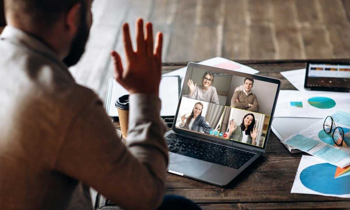 A person sitting at a desk, participating in a virtual meeting with team members displayed on a laptop screen, symbolizing gathering customer feedback through video calls.